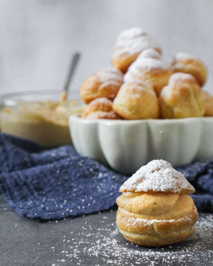 Boozy-Pumpkin-Cream-Puffs-with-Bowl-of-Pumpkin-Whipped-Cream-and-one-filled-cream-puff-out-front.j