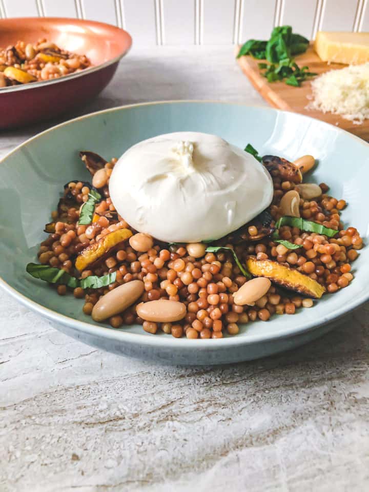 Burrata-with-lemony-couscous-in-big-blue-bowl-with-ingredients-in-background