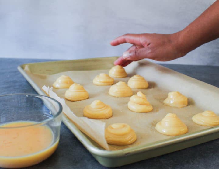 raw cream puff dough on baking sheet with hand