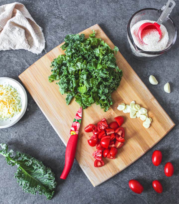 kale, tomatoes, and garlic on cutting board surrounded by ingredients