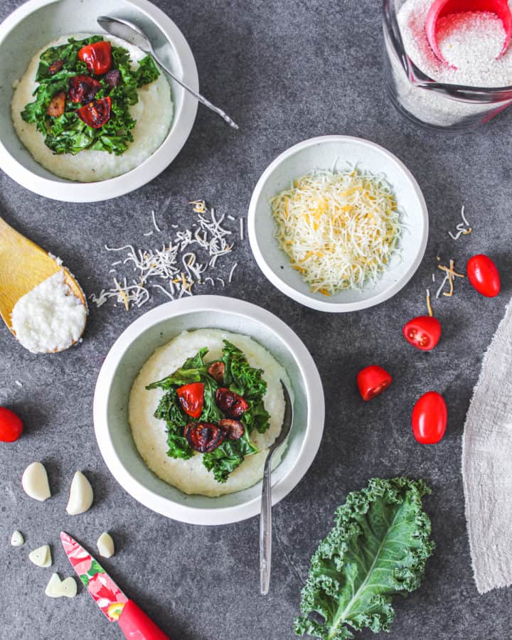 cheesy garlic grits with kale and tomatoes in bowl with spoon surrounded by ingredients