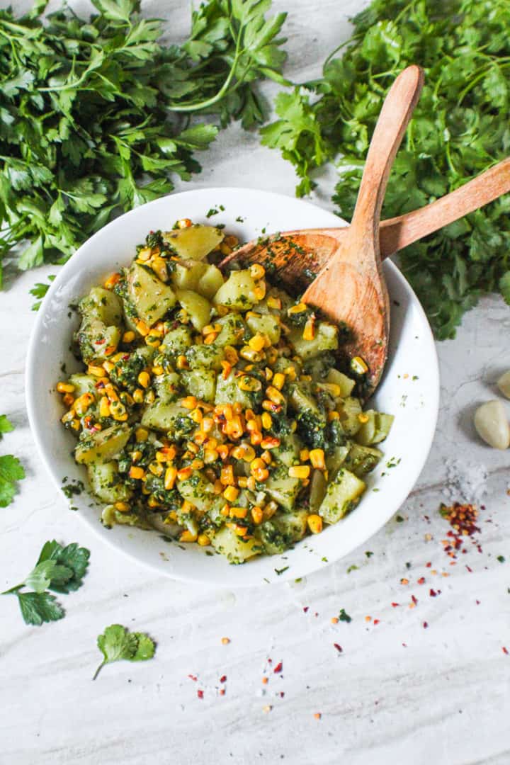 chimichurri potato salad in bowl with wooden utensils surrounded by cilantro