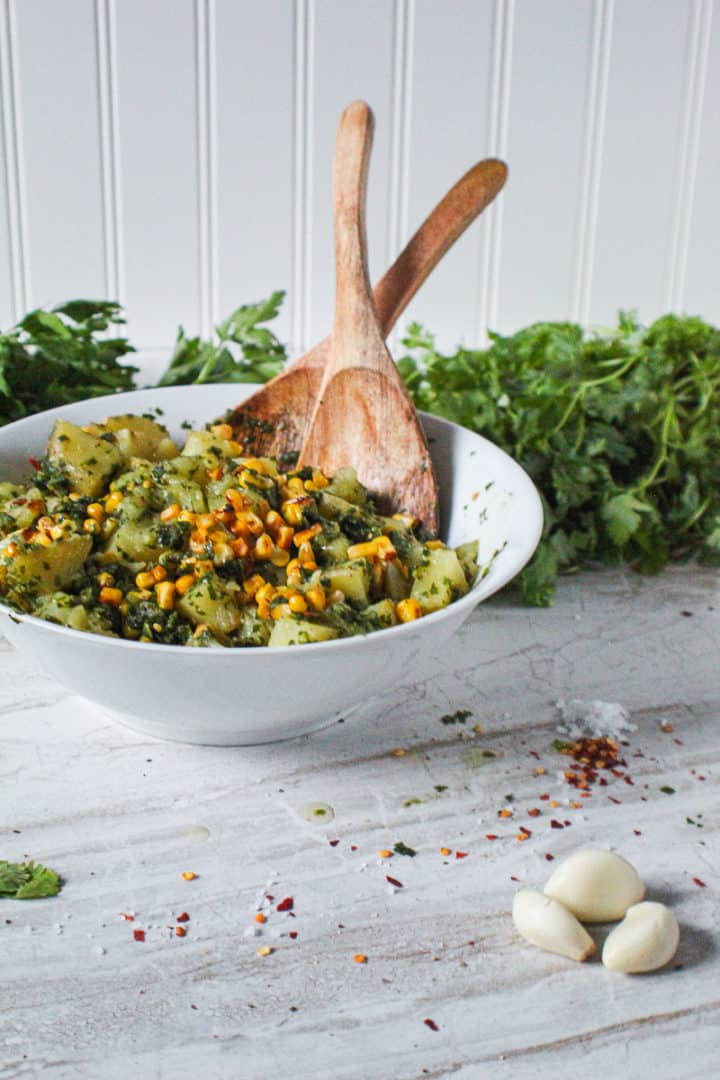 Side view of chimichurri potato salad with wooden utensils