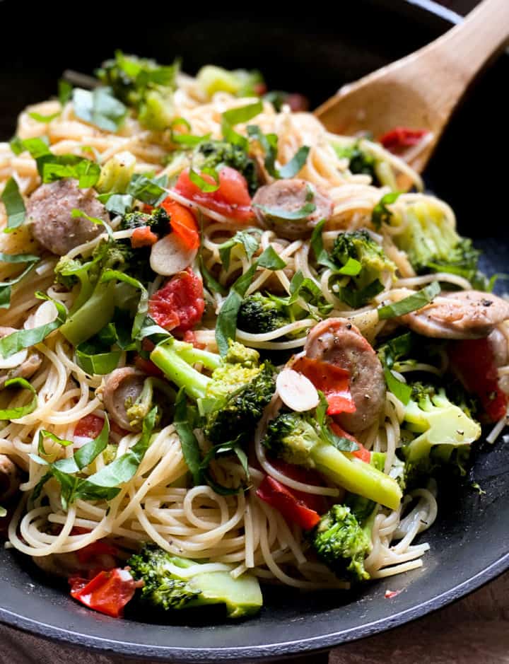 garlicky chicken sausage pasta with broccoli and tomatoes in bowl with wooden spoon