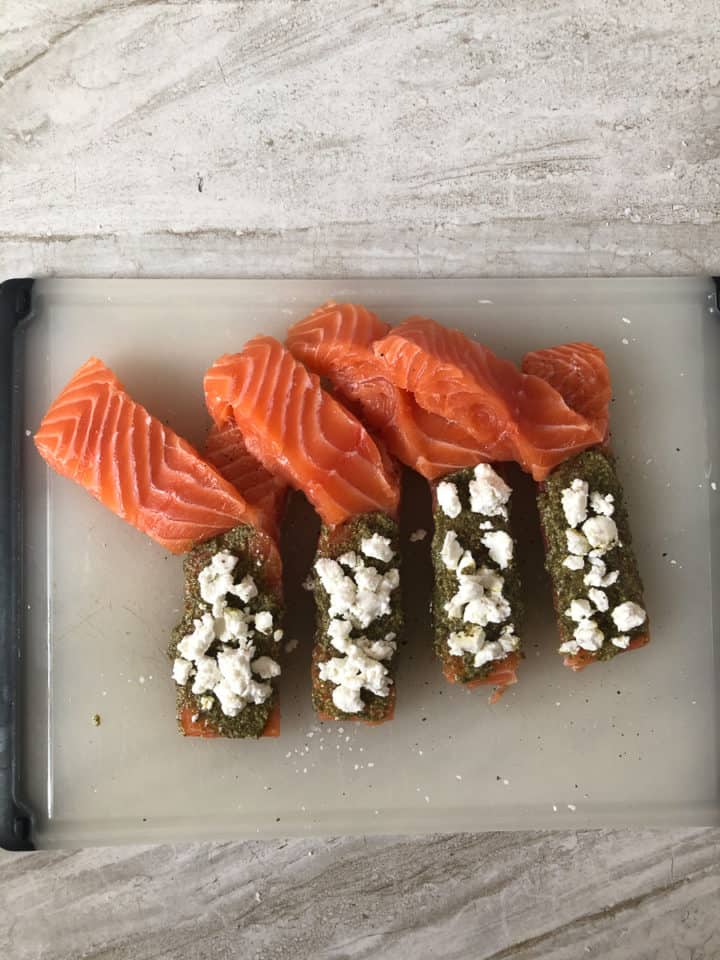 Raw halved salmon stuffed with pesto and goat cheese on baking sheet
