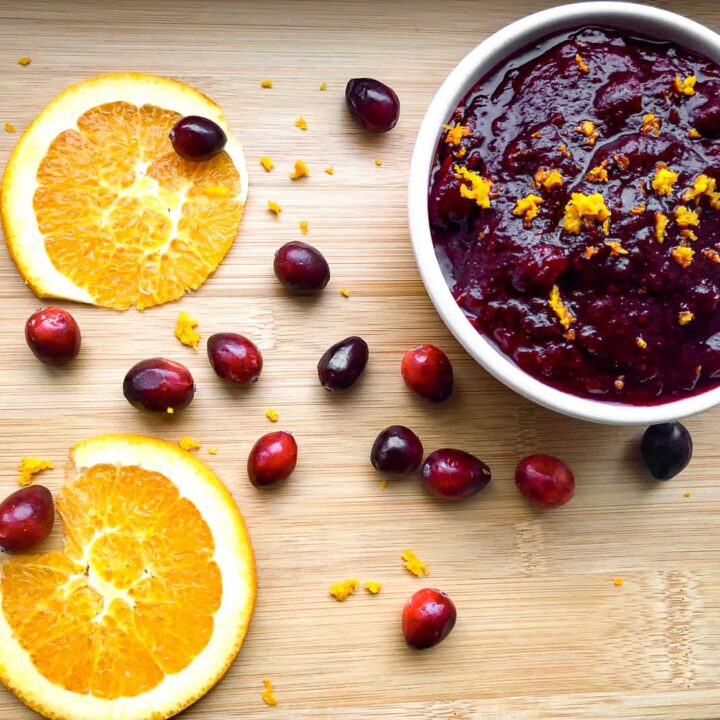 Orange cranberry sauce in bowl on table with fresh cranberries and orange slices