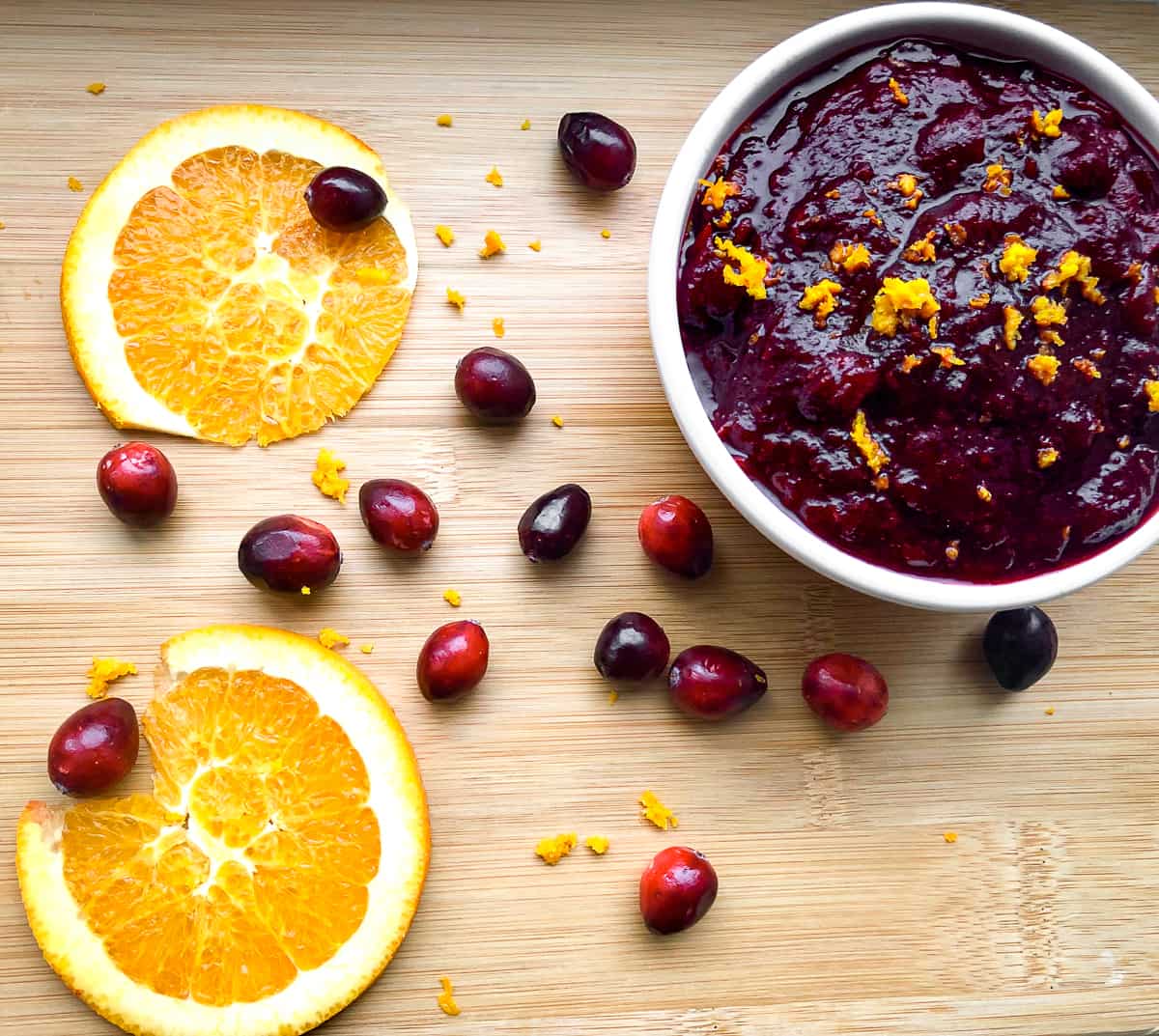 Orange cranberry sauce in bowl on table with fresh cranberries and orange slices 