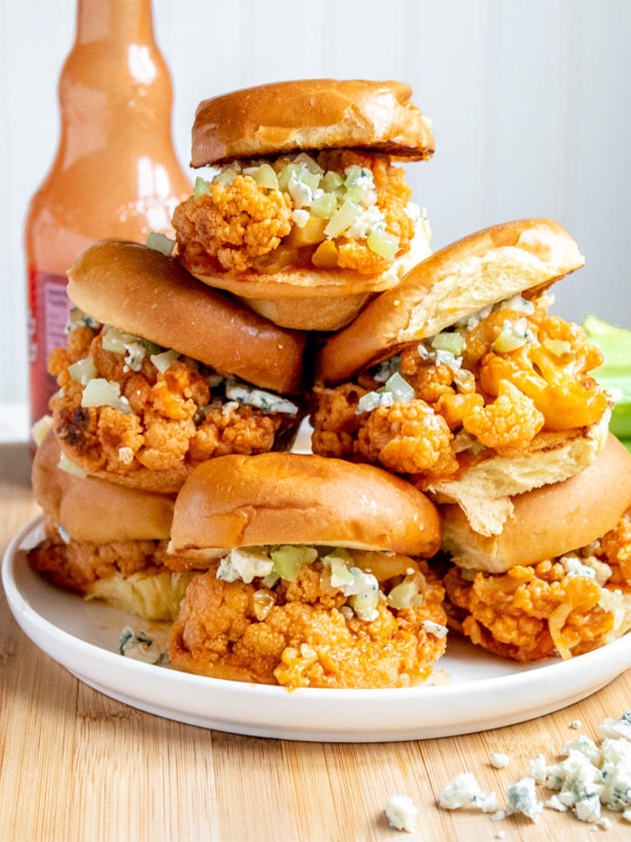 Four buffalo cauliflower sliders stacked on plate next a bottle of hot sauce