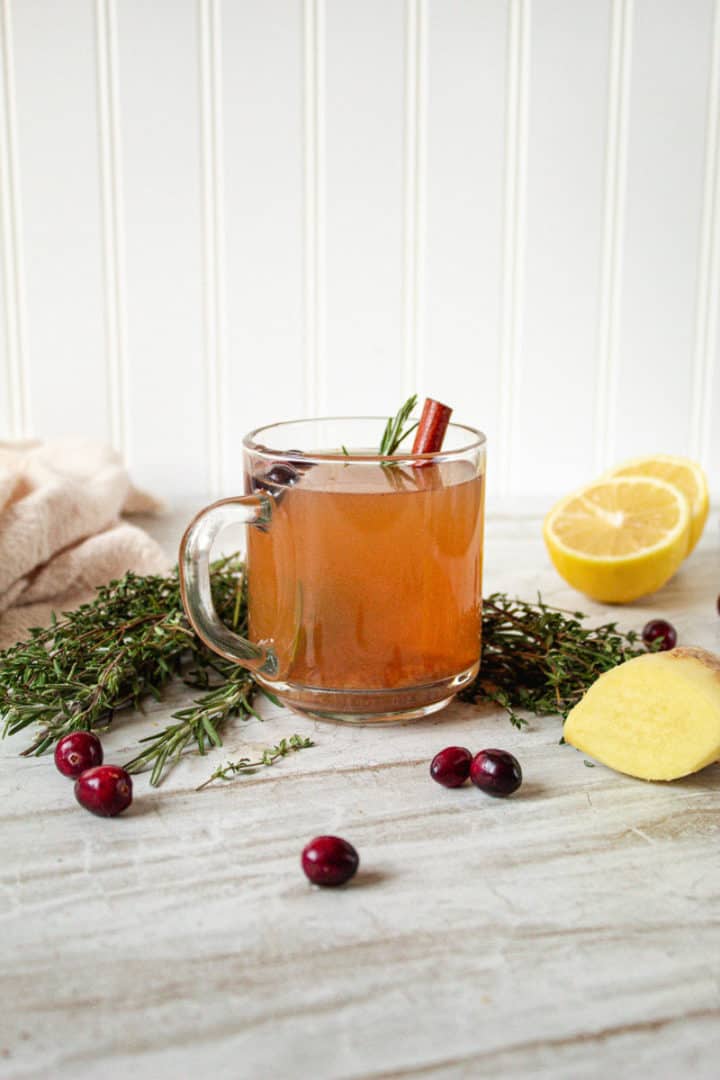 Single mug of herbed mulled cider surrounded by ingredients