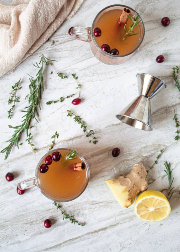 overhead shot of two mugs of herbed mulled cider surrounded by ingredients  and equipment