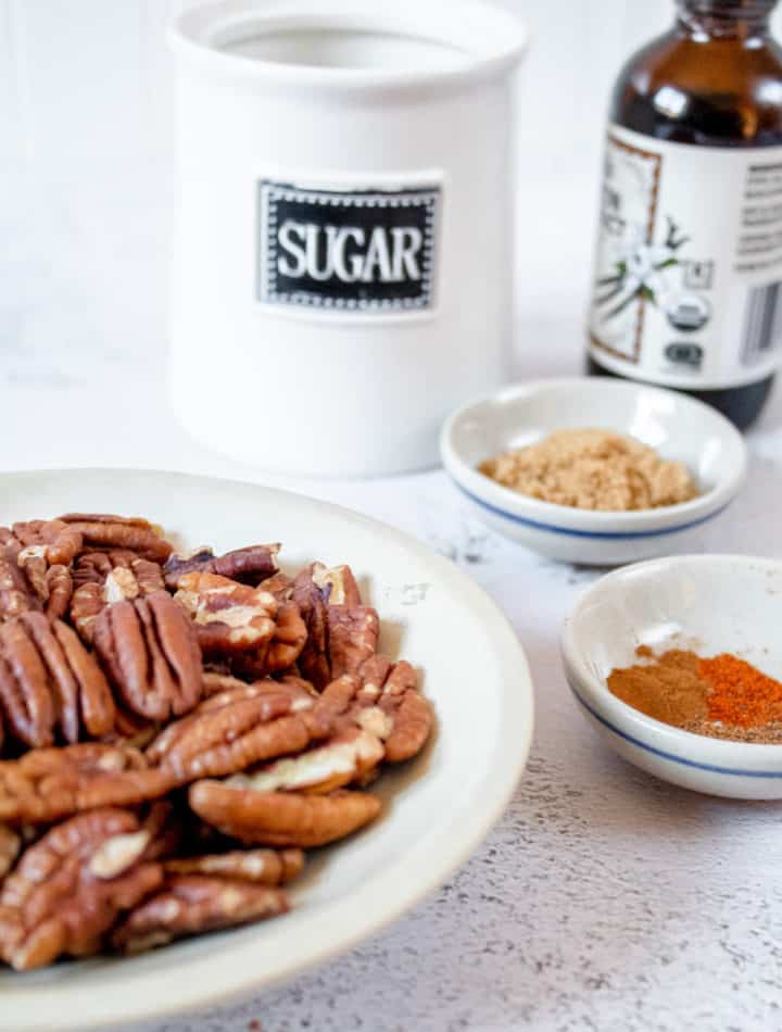 Spicy candied pecan ingredients (pecans, brown sugar, spices, sugar and vanilla extract) in separate containers