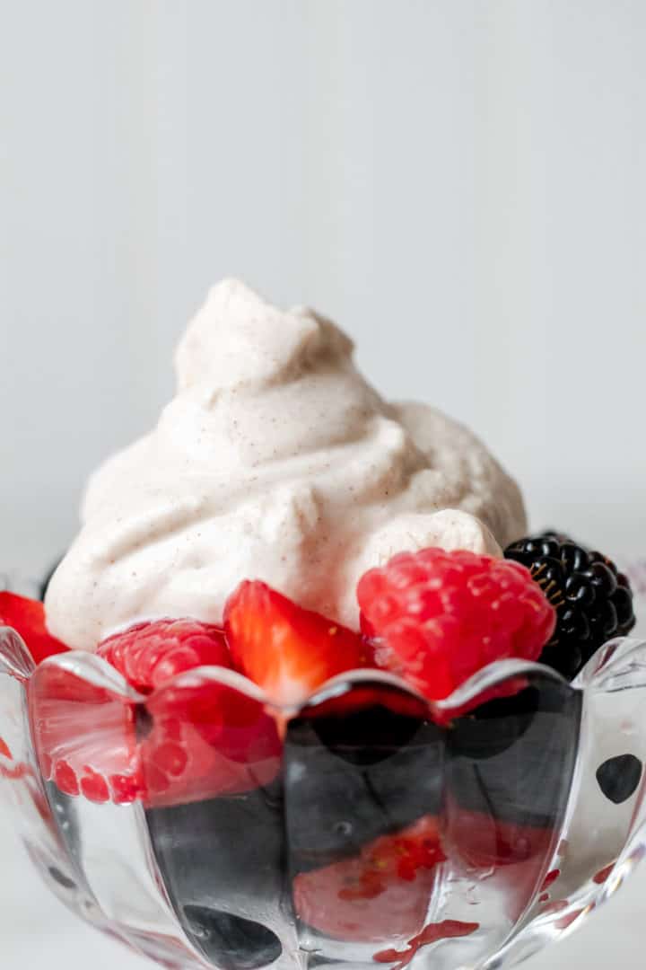 Drunken whipped cream topping on mixed berries in glass dish
