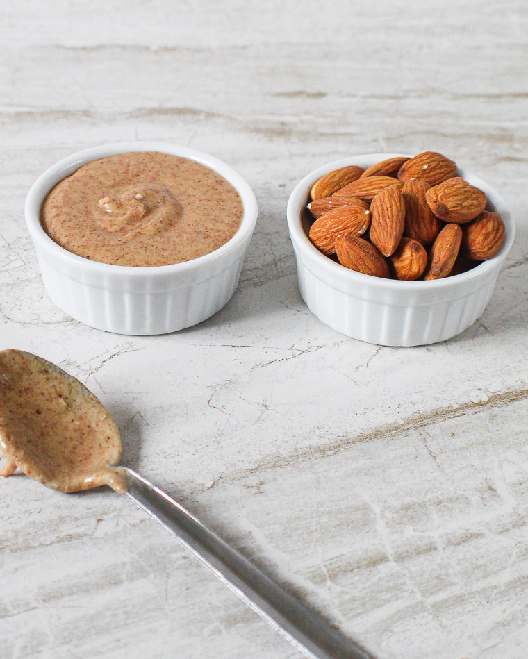 bowl of super easy almond butter next to a bowl of almonds next to a spoon